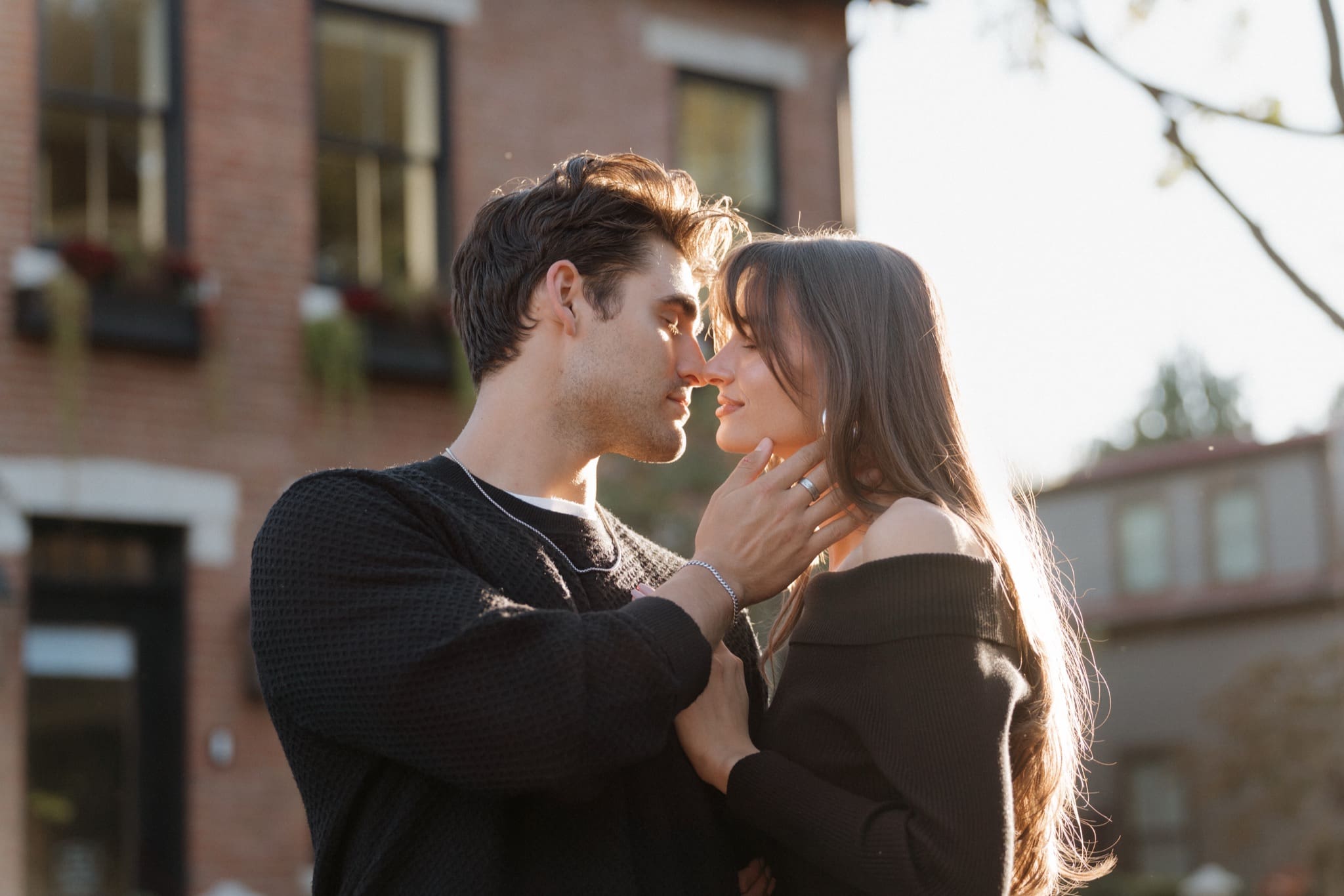 Couple leaning in for a kiss beside a red-brick home with window boxes in German Village, Columbus
