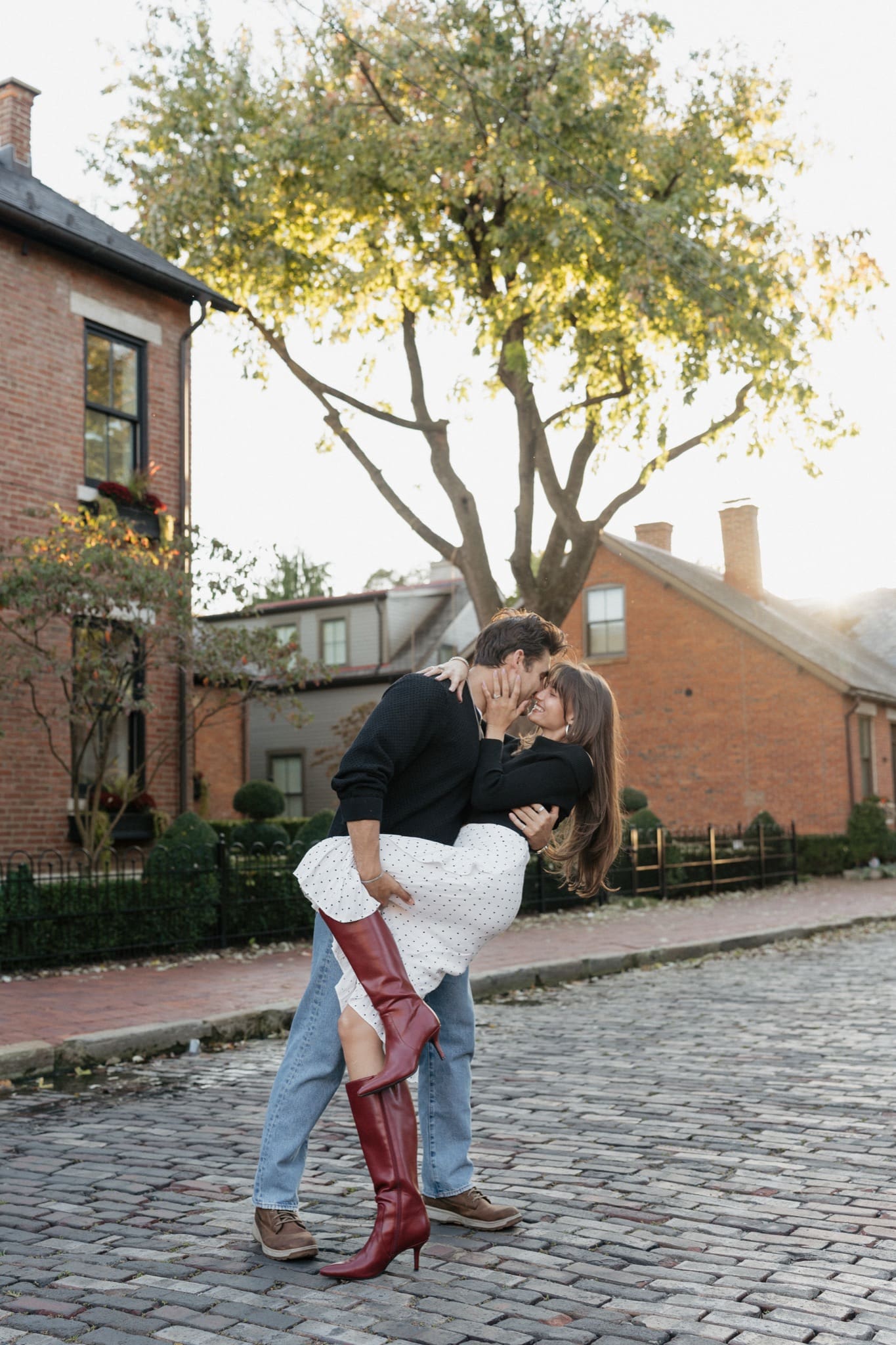 Man dipping his fiancée in red boots on a brick street in German Village, fall engagement session in Columbus, Ohio