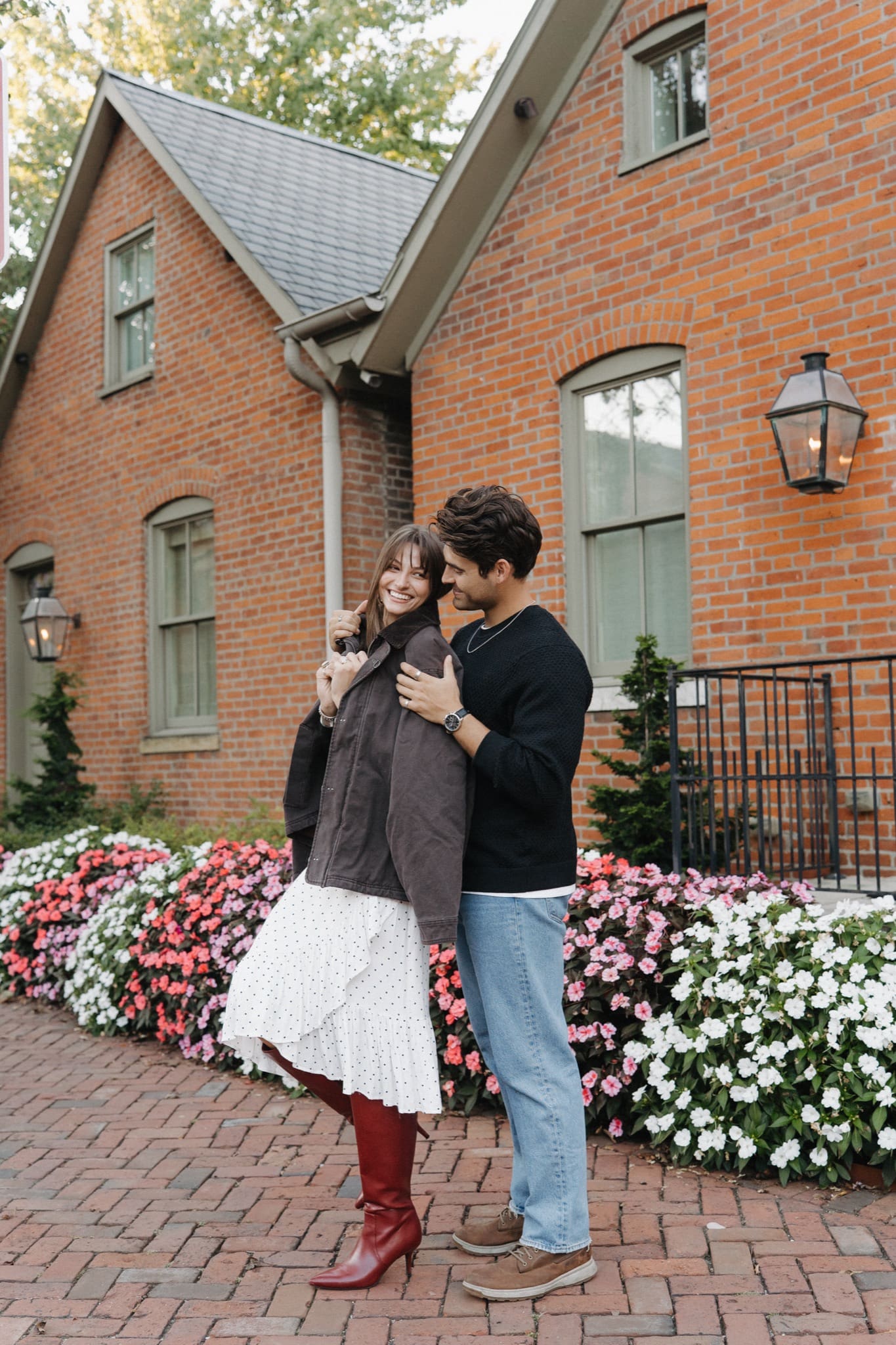 Couple embracing in front of a brick house and flower beds near Schiller Park, Columbus engagement photos