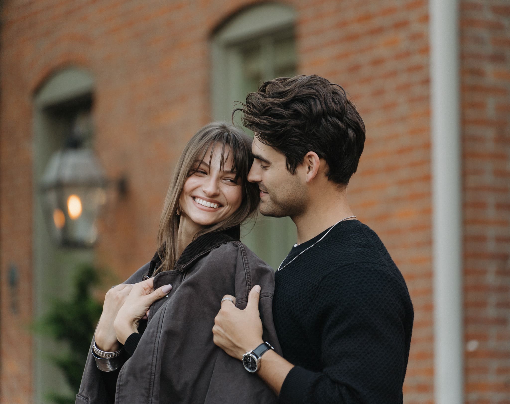 Smiling couple sharing a jacket in front of a brick wall and gas lantern in German Village, Columbus, Ohio